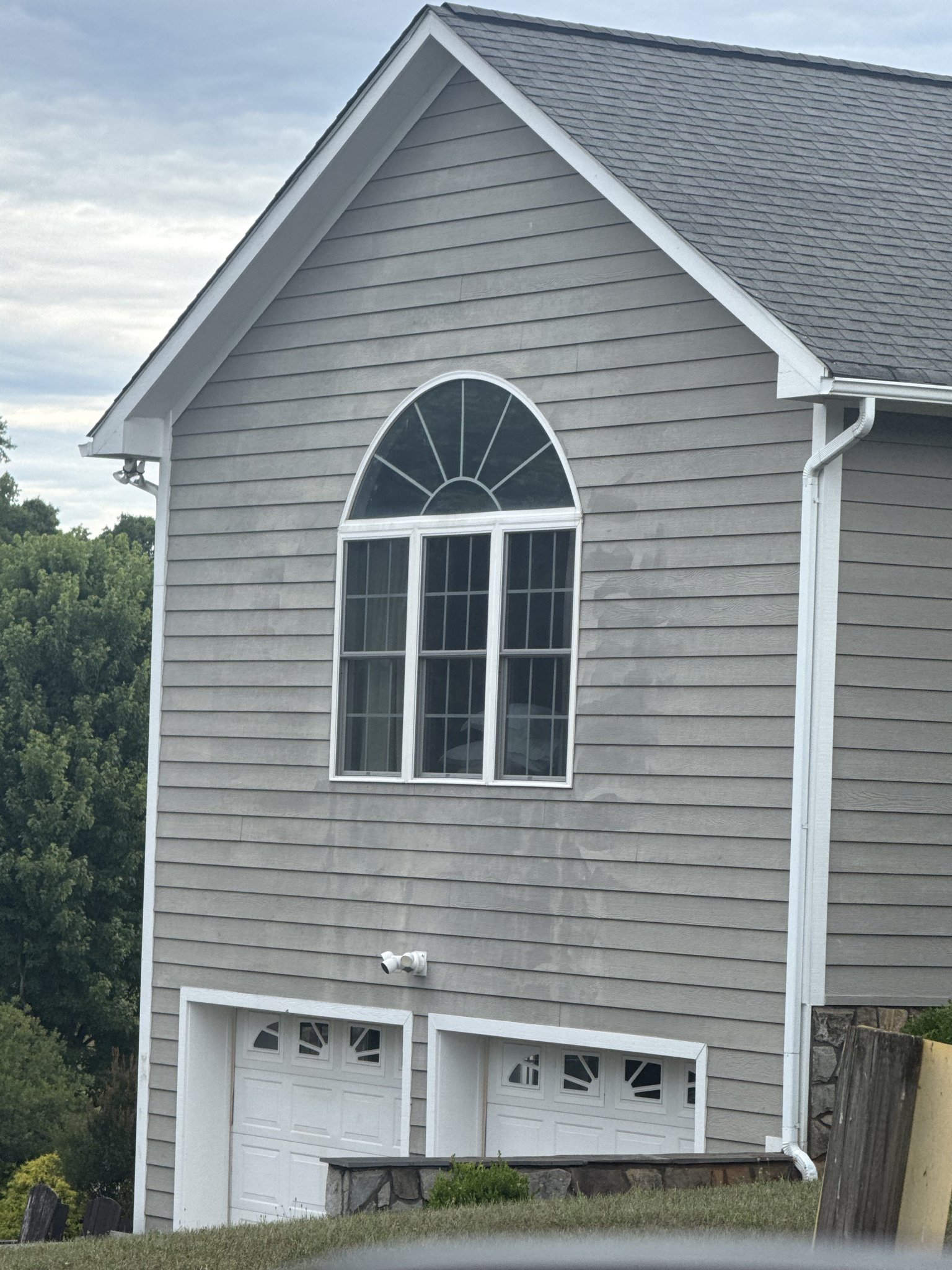 Streaks stripped into gray siding around a window by a pressure washer