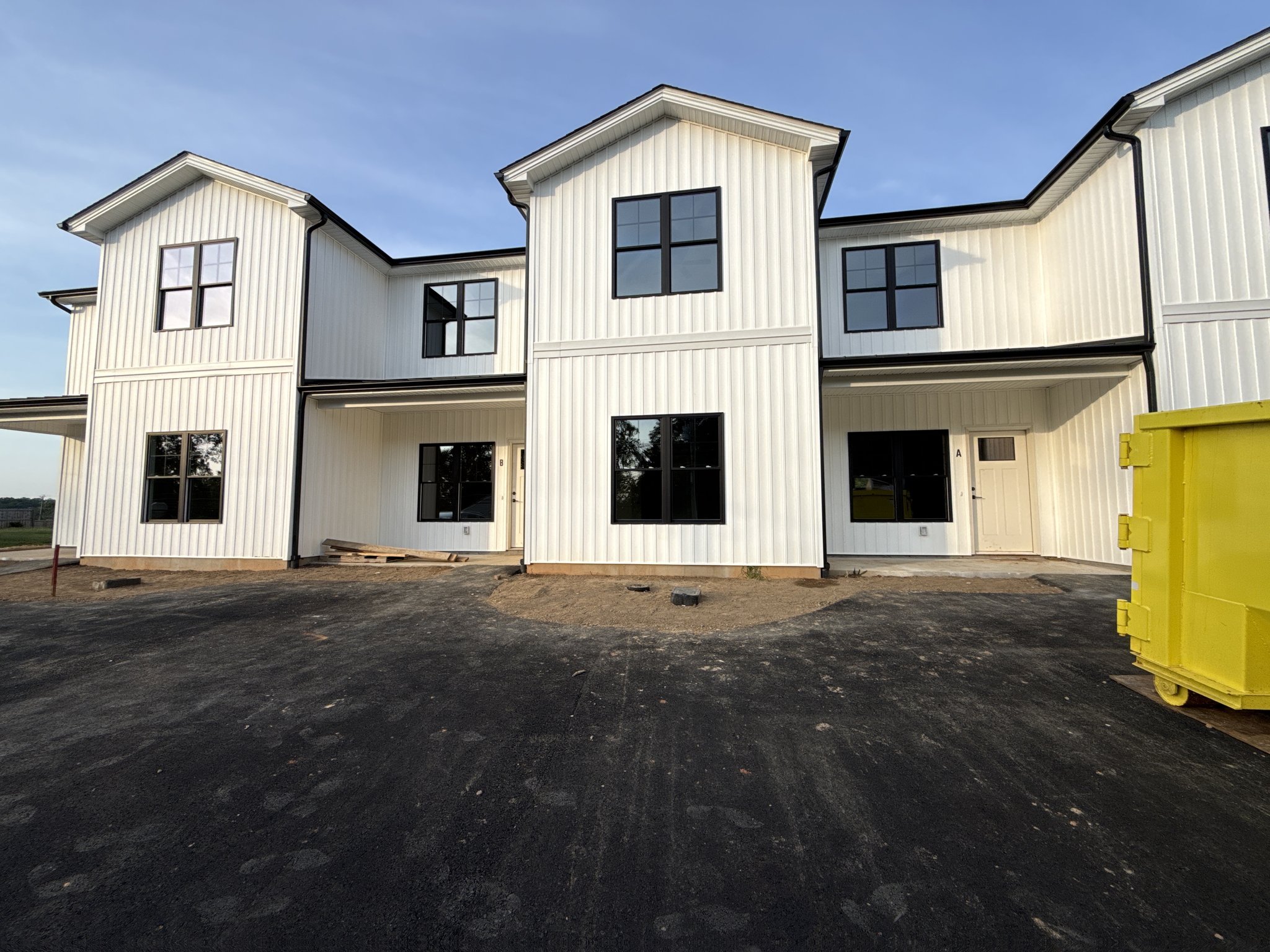 Front of the new triplex with bare graded soil and a construction dumpster still on site