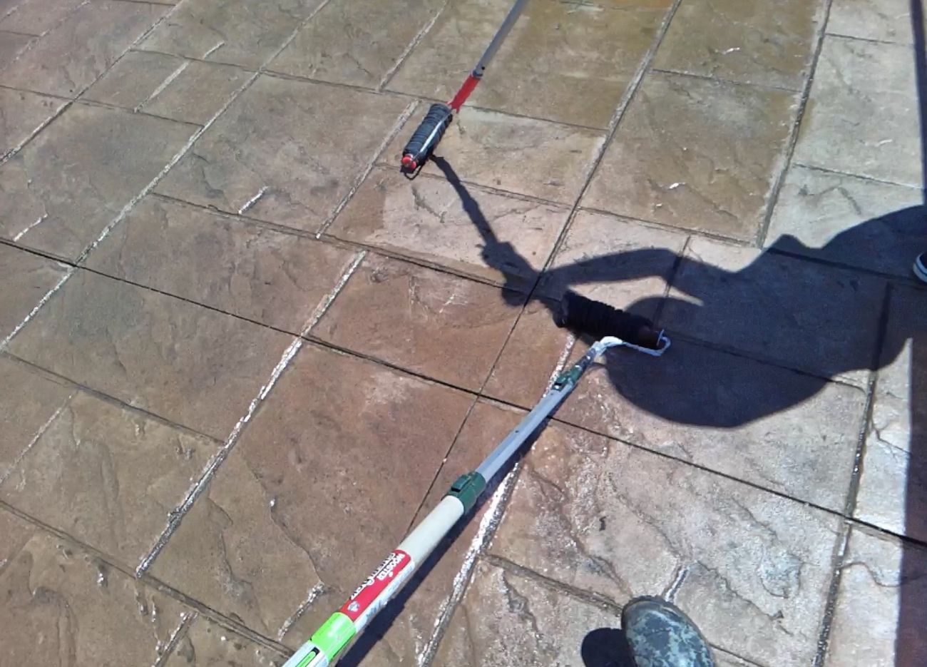 Rolling premium sealer onto stamped concrete driveway